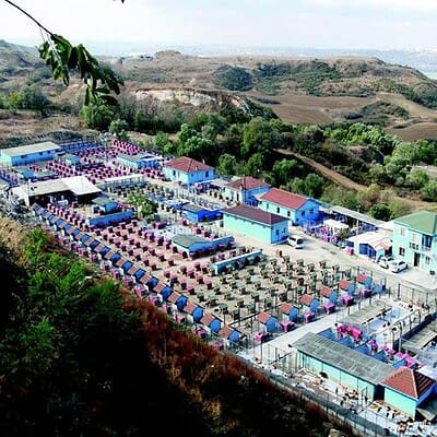 Kamp alanında renkli çadırlar ve konaklama alanları, doğa ile iç içe, geniş ve düzenli kamp alanı, yeşil ve mavi tonlarda yapıların bulunduğu turistik kamp merkezi.